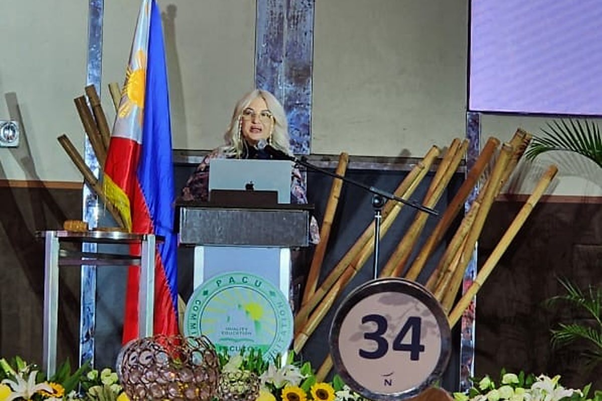 Dr. Ingrid Ursua addressing PACUCOA member institutions from the lectern, with AAG&rsquo;s presentation on screen